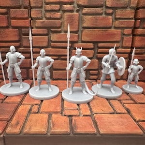 Puede incluir: Un conjunto de seis figuras en miniatura grises de soldados medievales. Cada figura está de pie sobre una base circular y sostiene una lanza o una espada. Las figuras están en varias poses, algunas con escudos.