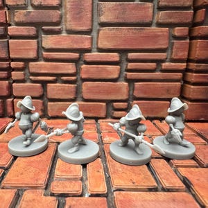 May include: Four gray miniature figurines of soldiers, each standing on a circular base. The soldiers wear helmets and hold weapons, posed against a brick wall background. The miniatures are likely for a tabletop game.