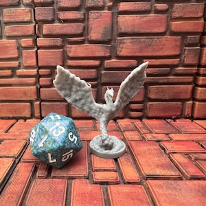 May include: A gray, 3D-printed phoenix figurine with outstretched wings stands next to a multi-sided die. The die is blue and green with white numbers. The background is a brick-like pattern in shades of brown and red.