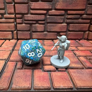 May include: A twenty-sided die with blue and green patterns and white numbers, next to a miniature figurine of a fantasy character. The figurine is grey and stands on a circular base. The background is a brick-like pattern.