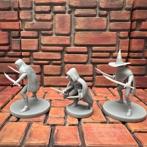 May include: Three gray miniature figures, each holding a sword, stand on circular bases. One figure wears a pointed hat. The figures are set against a brick wall and a tiled floor, suggesting a fantasy or tabletop game theme.