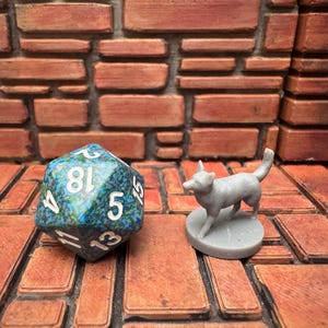 May include: A multi-sided die with white numbers and a blue and green marbled pattern sits next to a small grey wolf figurine. The objects are on a brick-like surface, suitable for tabletop gaming.