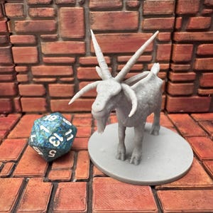 May include: A gray miniature goat figurine with large horns, standing on a gray circular base. A blue and white twenty-sided die is next to the goat. The background is a brick wall.