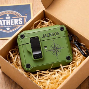 Può includere: Una custodia protettiva verde oliva per auricolari wireless, personalizzata con il nome "JACKSON" e un design a rosa dei venti. La custodia ha una chiusura nera e un moschettone, presentata in una confezione regalo di cartone con paglia decorativa.