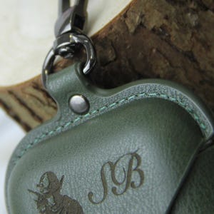 Op de afbeelding: Groene leren etui met een zilverkleurige sluiting. De etui heeft een reli&euml;f ontwerp van een conquistador en de initialen "SB". De stiksels zijn lichtgroen.
