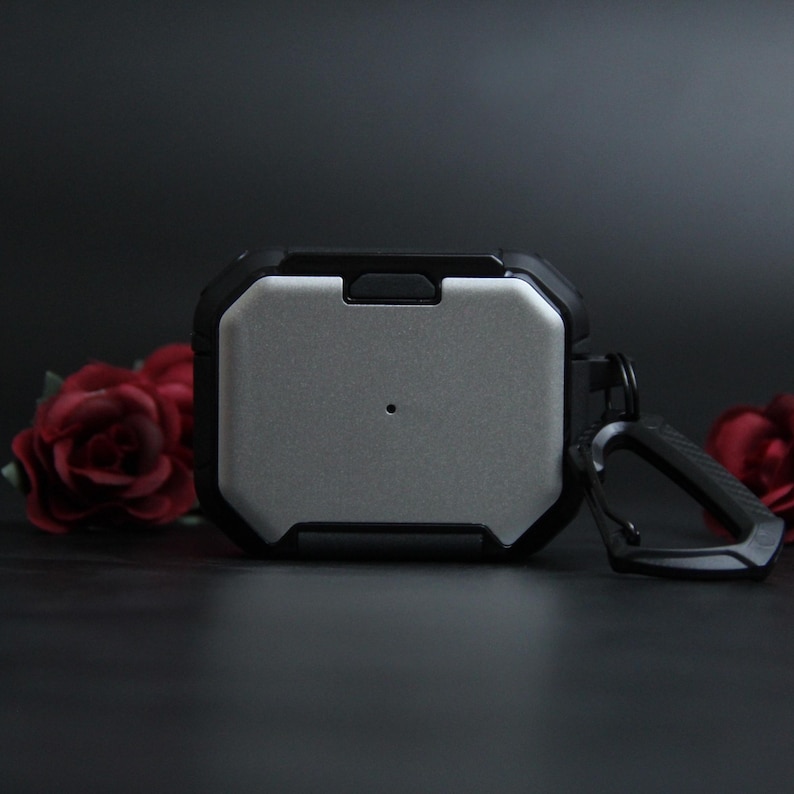 Puede incluir: Funda protectora para auriculares con un panel central plateado y un marco negro resistente. Incluye un mosquet&oacute;n para sujetar. Rosas rojas en el fondo.
