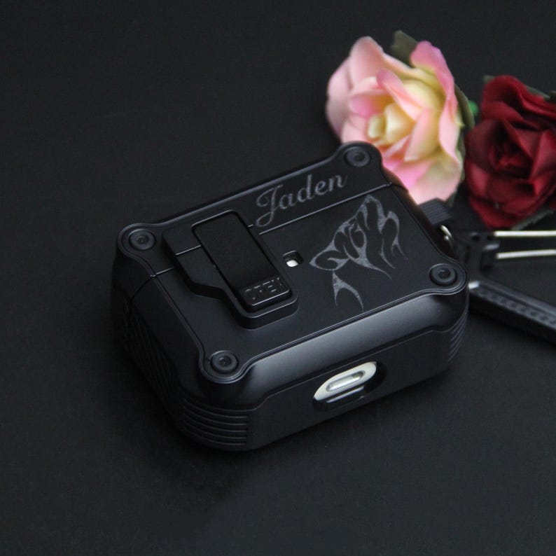 May include: Black protective case featuring a wolf design and the name "Jaden" engraved on the top. The case has a clip and a charging port. Pink and red roses are in the background.