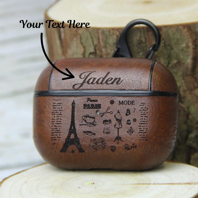 May include: Brown leather AirPod case with a black carabiner clip. The case is embossed with the name "Jaden" and Parisian-themed illustrations, including the Eiffel Tower and the word "Paris".