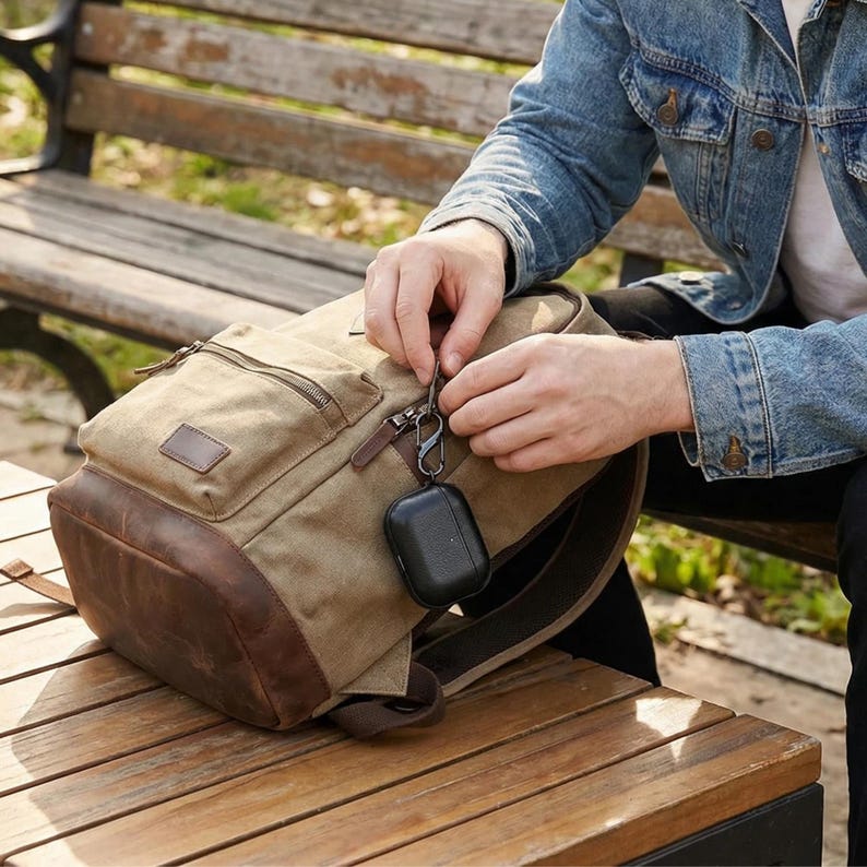 Peut inclure: Un sac &agrave; dos en toile beige avec des d&eacute;tails en cuir marron. Le sac &agrave; dos a plusieurs poches et une fermeture &eacute;clair. Un &eacute;tui noir pour &eacute;couteurs est attach&eacute; &agrave; la fermeture &eacute;clair. Le sac &agrave; dos est sur une surface en bois.