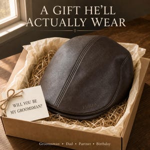 May include: A dark brown flat cap with the name JAMES embossed on the side, presented in a cardboard gift box with paper filler and a small white card tied with twine that reads WILL YOU BE MY GROOMSMAN? The text A GIFT HE'LL ACTUALLY WEAR is visible.