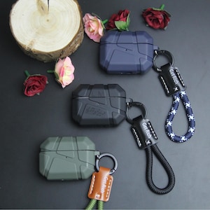 Pode incluir: Estojos protetores para fones de ouvido sem fio em azul escuro, preto e verde oliva. Cada estojo tem um design robusto e inclui um cordão com o texto "Get Rich".