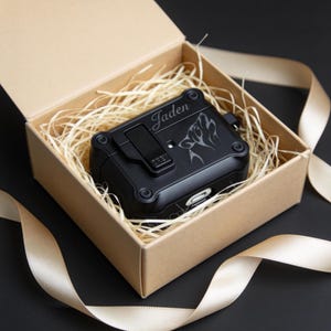 May include: A black protective case for wireless earbuds, personalised with the name "Jaden" and a wolf design, presented in a kraft paper gift box with decorative straw and a gold ribbon.
