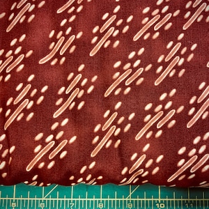 May include: A close-up of a brown fabric with a white geometric pattern. The pattern is made up of small white dots and diagonal lines.