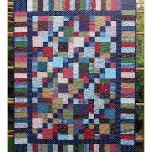May include: A quilt pattern called "Salt Water Taffy" made with fabrics from the "Scrap Happy" collection by Exclusively Quilters. The quilt is made up of a variety of colorful squares and rectangles, with a dark blue border.