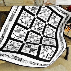 May include: Black and white quilt with a geometric pattern of stars and triangles. The quilt is made with a variety of fabrics and has a black border.