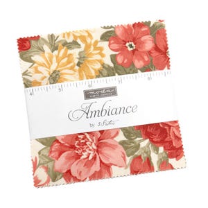May include: A stack of fabric squares with a floral pattern in shades of red, yellow, and green. The fabric is wrapped with a white label that reads "Ambience" by 3 Sisters. A ruler is printed on the label.