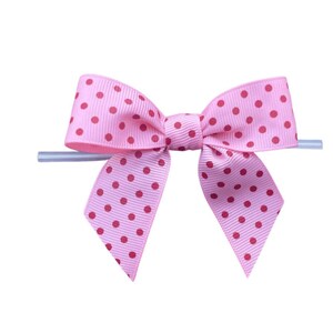 Op de afbeelding: Een roze strik met rode stippen. De strik is gemaakt van lint en heeft een klassieke vorm. Het is bevestigd aan een doorzichtige plastic stok, waarschijnlijk voor weergave of bevestiging.