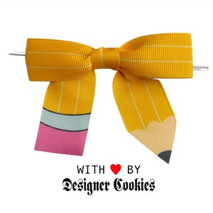 May include: A yellow ribbon bow designed to look like a pencil. The bow has a yellow and white striped pattern, with a pink, light blue, and yellow pencil tip design. The text "WITH ❤️ BY Designer Cookies" is at the bottom.