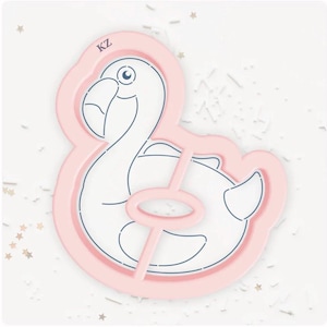 May include: A pink flamingo-shaped cookie cutter with a white interior and blue outline. The cutter has a handle and the letters "KZ" are visible. The design is on a white surface with star-shaped confetti.