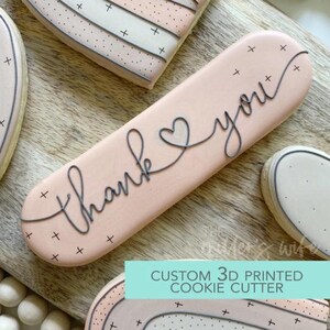 May include: A light pink cookie with the words "thank you" written in black script. The cookie is decorated with small black crosses. The text "CUSTOM 3D PRINTED COOKIE CUTTER" is at the bottom.