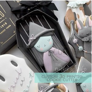 May include: A collection of Halloween-themed cookies. A witch-shaped cookie in a coffin-shaped box is the focal point. Other cookies include a ghost with "trick or treat" text, and a rabbit. The text "CUSTOM 3D PRINTED COOKIE CUTTER" is visible.