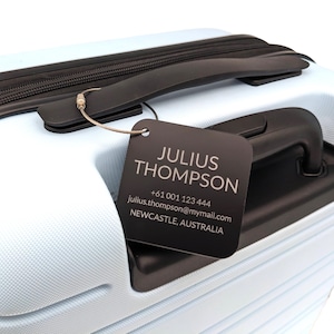 May include: A black luggage tag with the name Julius Thompson, phone number +61 001 123 444, email address julius.thompson@mymail.com, and location Newcastle, Australia.