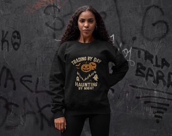 May include: Black sweatshirt with the text "TRADING BY DAY HAUNTING BY NIGHT" and a Halloween-themed graphic featuring pumpkins, bats, candles, and a ghost. The sweatshirt is worn by a person.