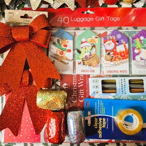 以下が含まれることがあります： クリスマスのギフトラッピング用品のコレクション。大きな赤いグリッターリボン、お祝いのイラストが描かれたギフトタグ、メタリックマーカー、透明粘着テープ、装飾リボンのロールが含まれています。クリスマスギフト包装も含まれています。