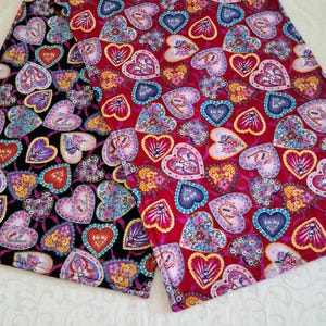 May include: Two fabric pieces with a heart pattern. One is black with hearts in red, purple, and blue. The other is red with hearts in pink, blue, and yellow. The hearts have floral and decorative designs.
