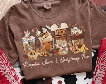 Può includere: T-shirt marrone con grafica di personaggi Disney e bevande alla zucca speziata. Il testo "Pumpkin Spice & Everything Nice" è stampato sotto. La maglietta è esposta su un motivo a pelle di mucca.