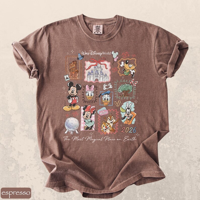 Op de afbeelding: Espresso-kleurig T-shirt met een collage van Disney-personages en bezienswaardigheden. Het ontwerp bevat Mickey Mouse, Minnie Mouse, Donald Duck en Goofy, samen met de tekst "Walt Disney World" en "2026". Het shirt heeft ook de tekst "The Most Magical Place on Earth".