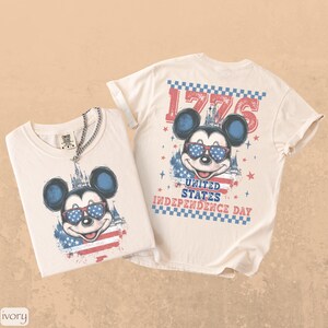 Puede incluir: Dos camisetas color marfil con un dise&ntilde;o patri&oacute;tico de Mickey Mouse. Una muestra a Mickey con gafas de sol con dise&ntilde;o de bandera. La otra tiene el texto "1776" y "United States Independence Day".
