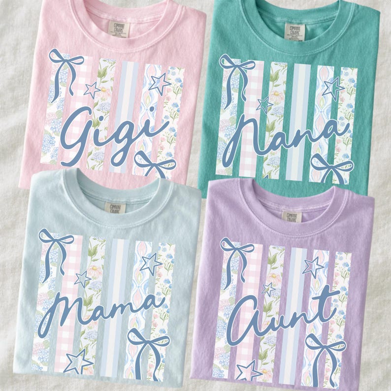 May include: Four pastel-colored t-shirts with the names "Gigi", "Nana", "Mama", and "Aunt" in cursive script. Each shirt features a vertical design with floral, gingham, and striped patterns, accented with bows and stars. The shirts are light pink, teal, light blue, and lavender.