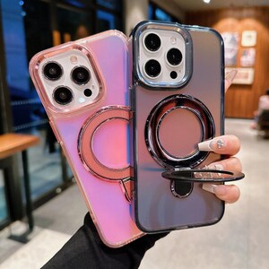 以下が含まれることがあります： リングホルダー付きのiPhoneケース2つ。左側のケースはピンクで虹色。右側のケースは黒で虹色です。