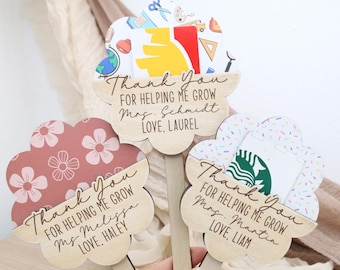 Op de afbeelding: Drie houten bloemvormige cadeaubonnenhouders met de tekst "Thank You For Helping Me Grow" en gepersonaliseerde namen. Eén heeft een bloemenpatroon, een andere schoolspullen en de derde een Starbucks-logo.