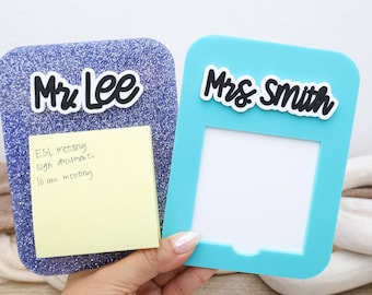 Op de afbeelding: Twee rechthoekige bureau-organizers met afgeronde hoeken. De ene is paars glitter met de tekst Mr. Lee en een geel memoblaadje. De andere is effen turquoise met de tekst Mrs. Smith en een witte vierkante uitsparing voor notities of foto's.