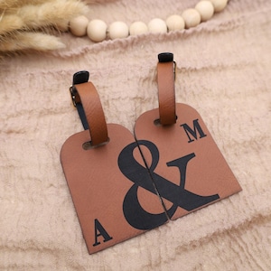 May include: Two brown leather luggage tags with black ampersand and letter designs. The tags are connected together and say "A & M" on them.