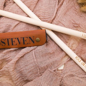 May include: Two wooden drumsticks with the text "I Love You!" and "Rock On Mike!" engraved on them. A brown leather drumstick holder with the name "Steven" engraved on it.