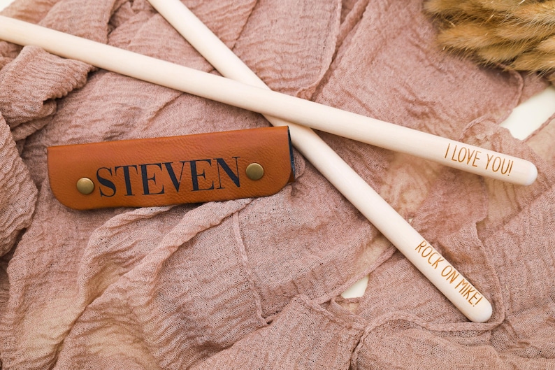 May include: Two wooden drumsticks with the text "I Love You!" and "Rock On Mike!" engraved on them. A brown leather drumstick holder with the name "Steven" engraved on it.