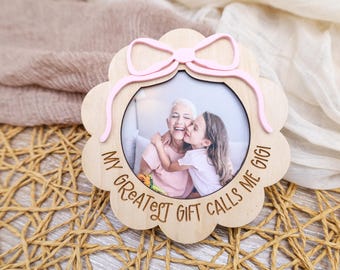 May include: Wooden photo frame with a pink bow and the text "My Greatest Gift Calls Me Gigi!" A photo of a grandmother and granddaughter is in the frame.