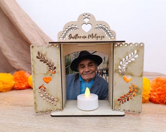 May include: A wooden memorial box with a photo of a man wearing a hat and a blazer. The box has decorative cutouts, including a heart and the name "Guillermo Melgoza". A battery-operated candle sits in front of the photo.