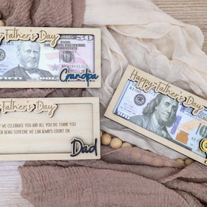 May include: Wooden Father's Day gift boxes with dollar bills inside. The boxes have laser-cut text that says "Happy Father's Day", "Grandpa", and "Dad". One box has a yellow trophy that says "Best Dad".