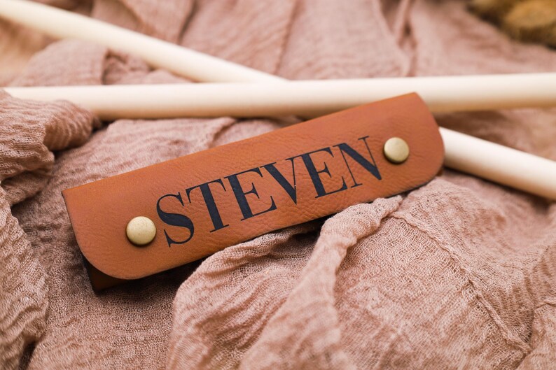 May include: A brown leather strap with the name "STEVEN" embossed in black lettering. The strap has two brass rivets.