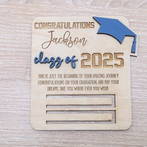 May include: Wooden graduation card with a blue graduation cap, the text "Congratulations Jackson class of 2025" and the message "This is just the beginning of your amazing journey Congratulations on your graduation, and may your dreams take you where ever you wish".