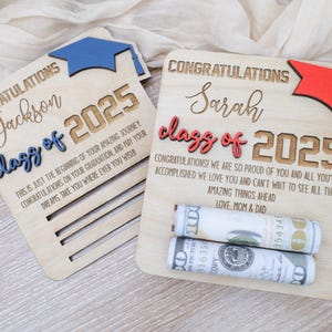 May include: Two wooden graduation signs with a blue and red graduation cap on each. The signs say "Congratulations Jackson class of 2025" and "Congratulations Sarah class of 2025". The signs have a slot for money to be inserted.