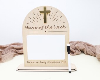 Op de afbeelding: Houten "Verse of the Week" bord met een gouden kruis en een wit whiteboard. Het bord heeft de tekst "Verse of the Week" en "The Martinez Family - Established 2026". Een zwart-witte marker is inbegrepen.