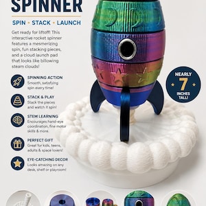 May include: A multi-colored, gradient-finished rocket spinner toy standing nearly 7 inches tall. The rocket consists of stackable segments in shades of green, purple, and blue, featuring star and moon cutouts, resting on a white cloud-shaped base.