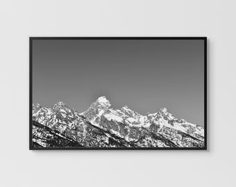 May include: Black and white framed print of a mountain range. The peaks are covered in snow, and the sky is a solid gray. The frame is black, and the print is mounted on a white wall.