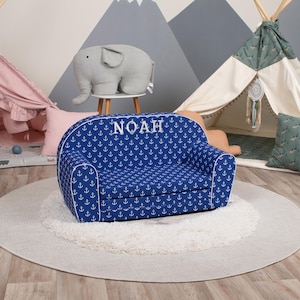 May include: A blue children's sofa with white anchor patterns and the name "NOAH" embroidered in white. The sofa has rounded arms and white piping. The sofa sits on a round, light gray rug.