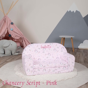 May include: Pink children's sofa with a unicorn print and the name "Isabella" embroidered on the back. The sofa is on a white rug in a room with a teepee and a small table.
